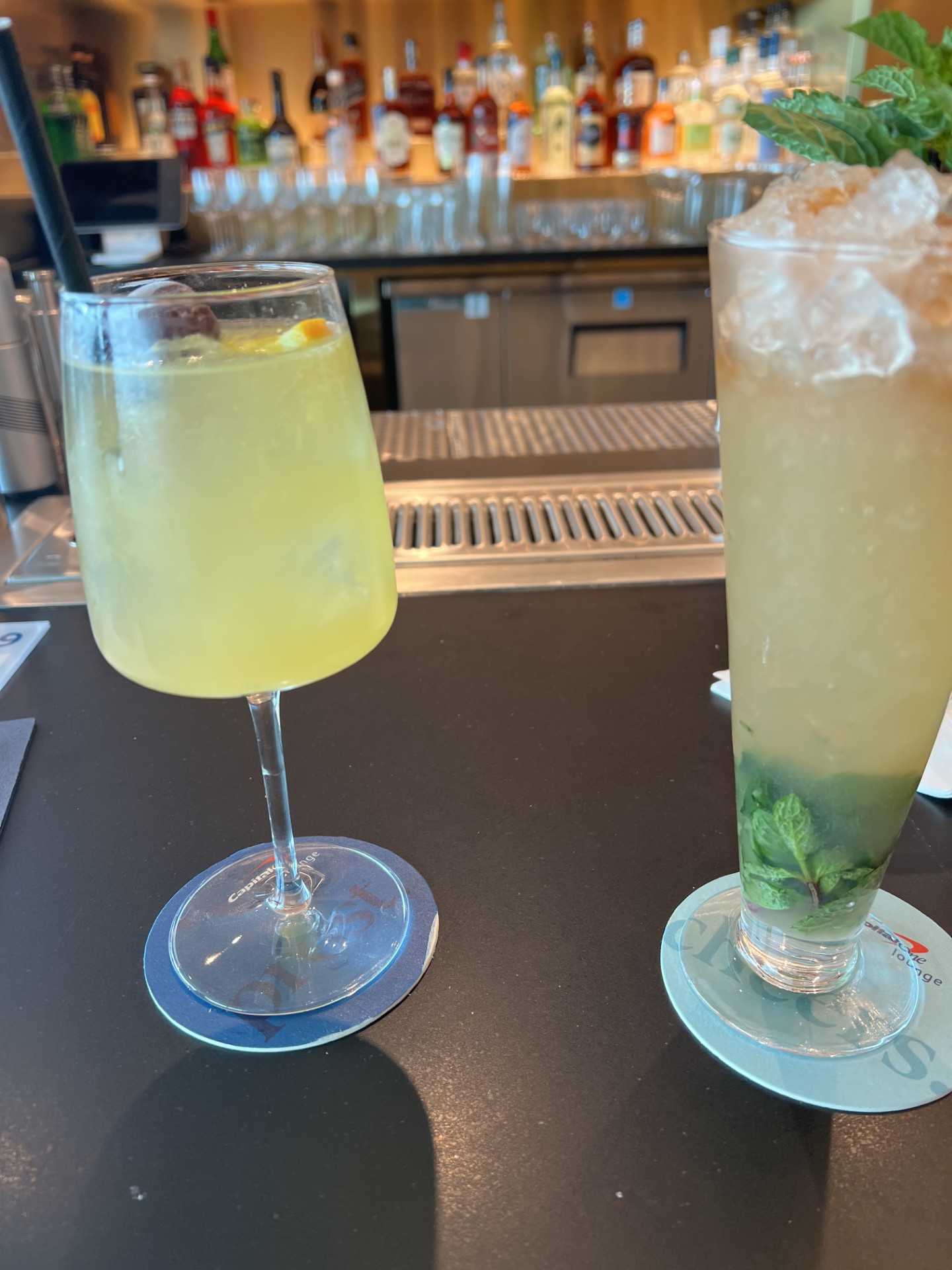 Two cocktails on a table with the bar in the background.
